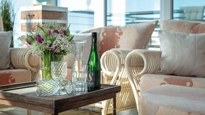 Una bandeja con una botella, vasos y flores sobre una mesa en una habitación con vistas a un edificio.