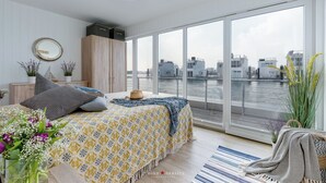 Un dormitorio moderno con un ventanal grande que da a una masa de agua, una cama con ropa de cama estampada y vistas a la ciudad.