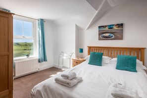 A bedroom with a bed, a window with a view of a landscape, a radiator, and a painting on the wall.