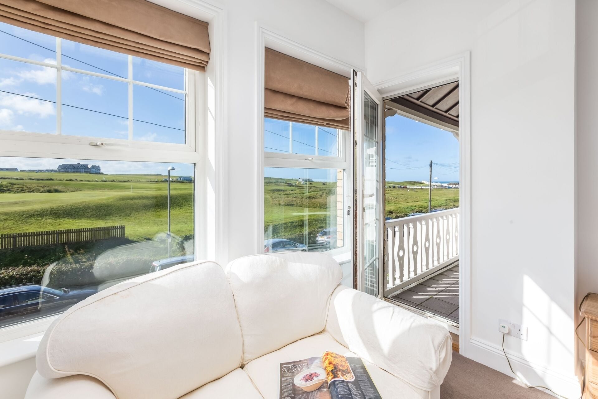 Una habitación con un sofá de cuero blanco, una revista y vistas a un paisaje verde a través de amplios ventanales.