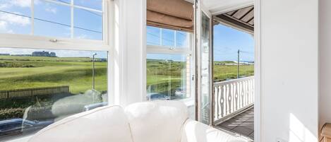 A room with a white leather sofa, a magazine, and a view of a green landscape through large windows.