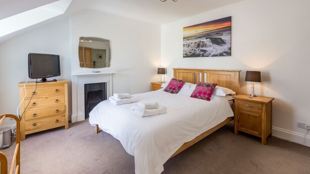 A bedroom with a large bed, a fireplace, a television, and a painting of a sunset. - Foreshore - sleeps 16 guests  in 9 bedrooms (Bude)