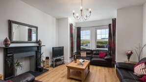A living room with a fireplace, a television, leather sofas, a coffee table, and a large window with curtains. - Foreshore - sleeps 16 guests  in 9 bedrooms (Bude)