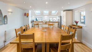 A spacious dining area with a long wooden table and chairs, a kitchen in the background, and skylights on the ceiling. - Foreshore - sleeps 16 guests  in 9 bedrooms (Bude)