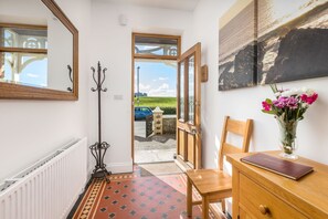A hallway with a radiator, a coat stand, a wooden chair, a wooden table with a book, and a vase with flowers.