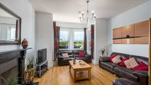 A modern living room with a fireplace, leather sofas, a wooden coffee table, and a large window with curtains. - Foreshore - sleeps 16 guests  in 9 bedrooms (Bude)