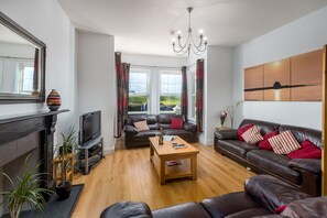 Ein modernes Wohnzimmer mit Kamin, Ledersofas, einem Holztisch und einem großen Fenster mit Vorhängen.
