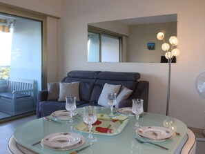 Un comedor con una mesa de vidrio dispuesta para cuatro personas, un sofá gris con cojines y una lámpara de pie con múltiples bombillas.