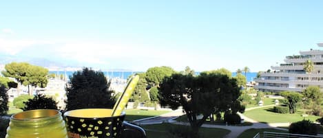 A view from a balcony overlooking a coastal area with a clear sky, a golf course, and a building with multiple balconies.