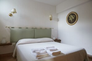 Una cama bien tendida con sábanas y toallas blancas, un cabecero verde y dos lámparas adosadas a la pared.
