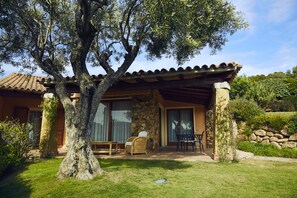 Una casa con fachada de piedra, un porche cubierto con mobiliario exterior y un árbol grande en primer plano.