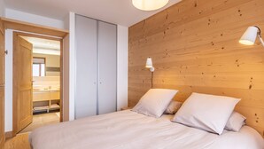 A bedroom with a large bed, wooden wall paneling, two bedside lamps, and a closet with a mirror.
