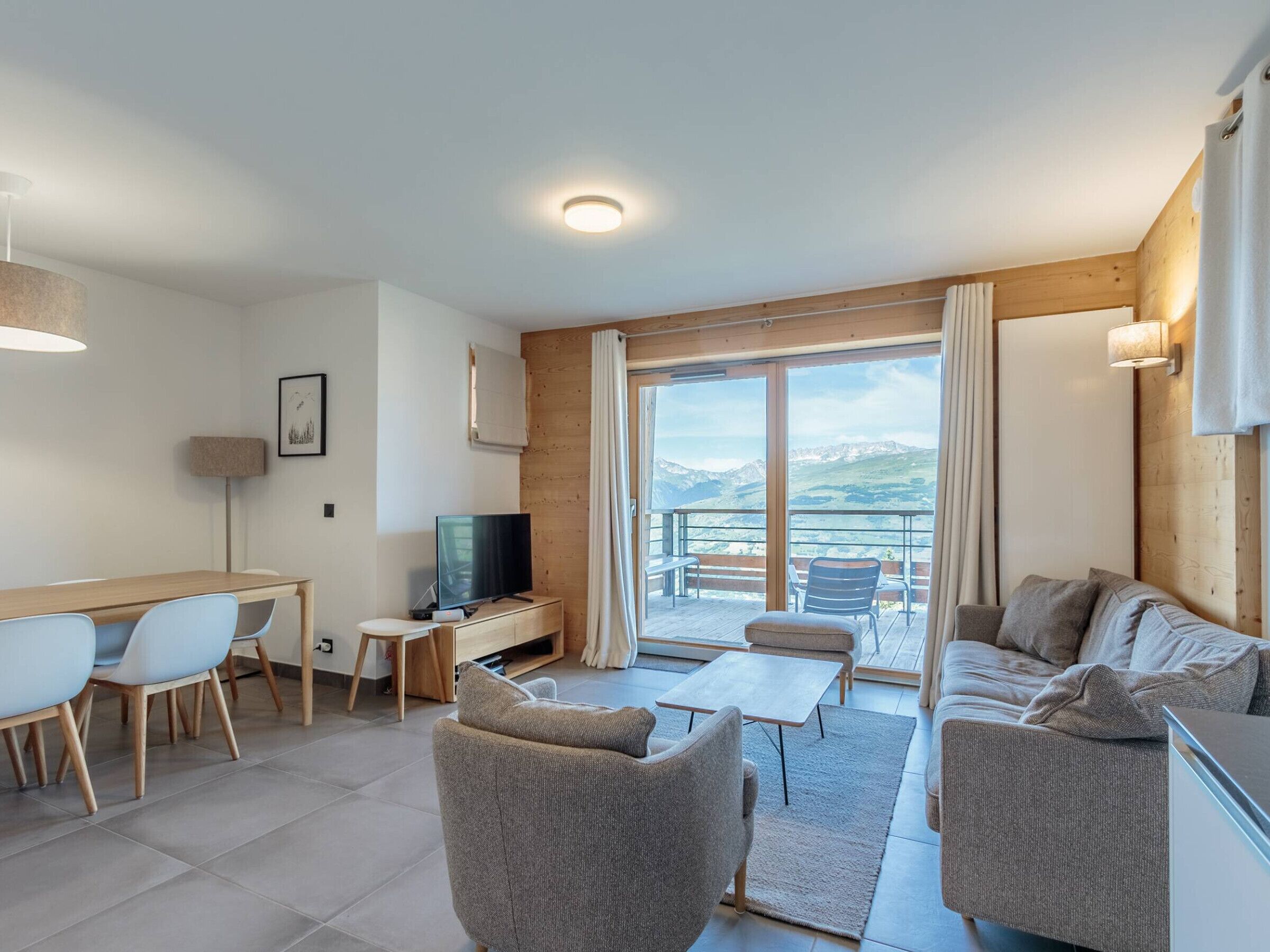 A modern living room with a TV, seating, and a balcony with a mountain view.