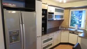 A compact kitchen with a built-in refrigerator, microwave, and oven. It features a black countertop, white cabinets, and a window providing natural light. - Bergspitze (Garmisch-Partenkirchen)