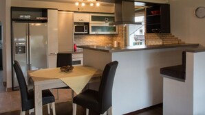 A modern kitchen with a central island, built-in appliances, and a dining area with a table and chairs. - Bergspitze (Garmisch-Partenkirchen)