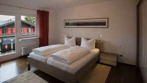 A modern bedroom with a large bed, bedside tables, a framed picture on the wall, and a view of a building outside. - Bergspitze (Garmisch-Partenkirchen)