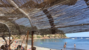 A beachside restaurant with outdoor seating under a thatched roof, overlooking a beach with people sunbathing and swimming. - Peaceful charming paradise, beach at 70m, private swimming pool,  plancha (La Seyne-sur-Mer)