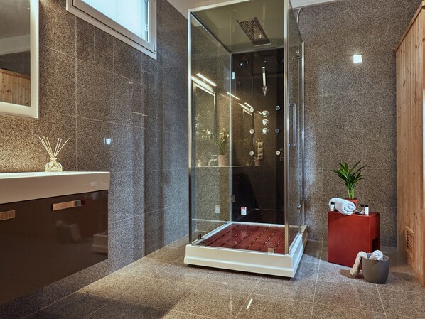Une salle de bain moderne avec une douche à parois de verre, des carreaux de granit, un banc en bois, un tabouret rouge et une plante en pot.
