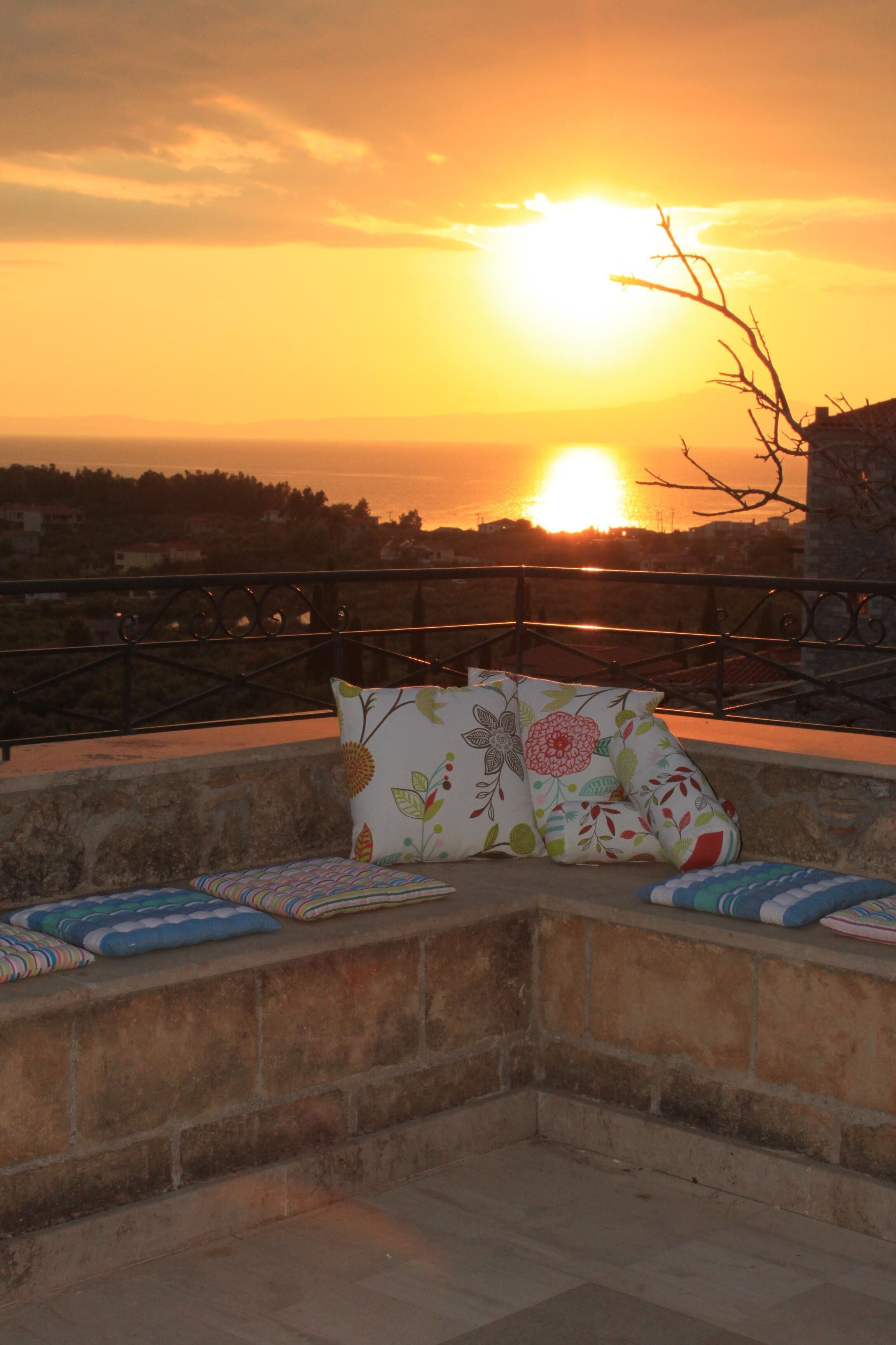 Ein Balkon mit Blick auf den Sonnenuntergang über dem Meer, mit einer Steinmauer und einem Metallgeländer.