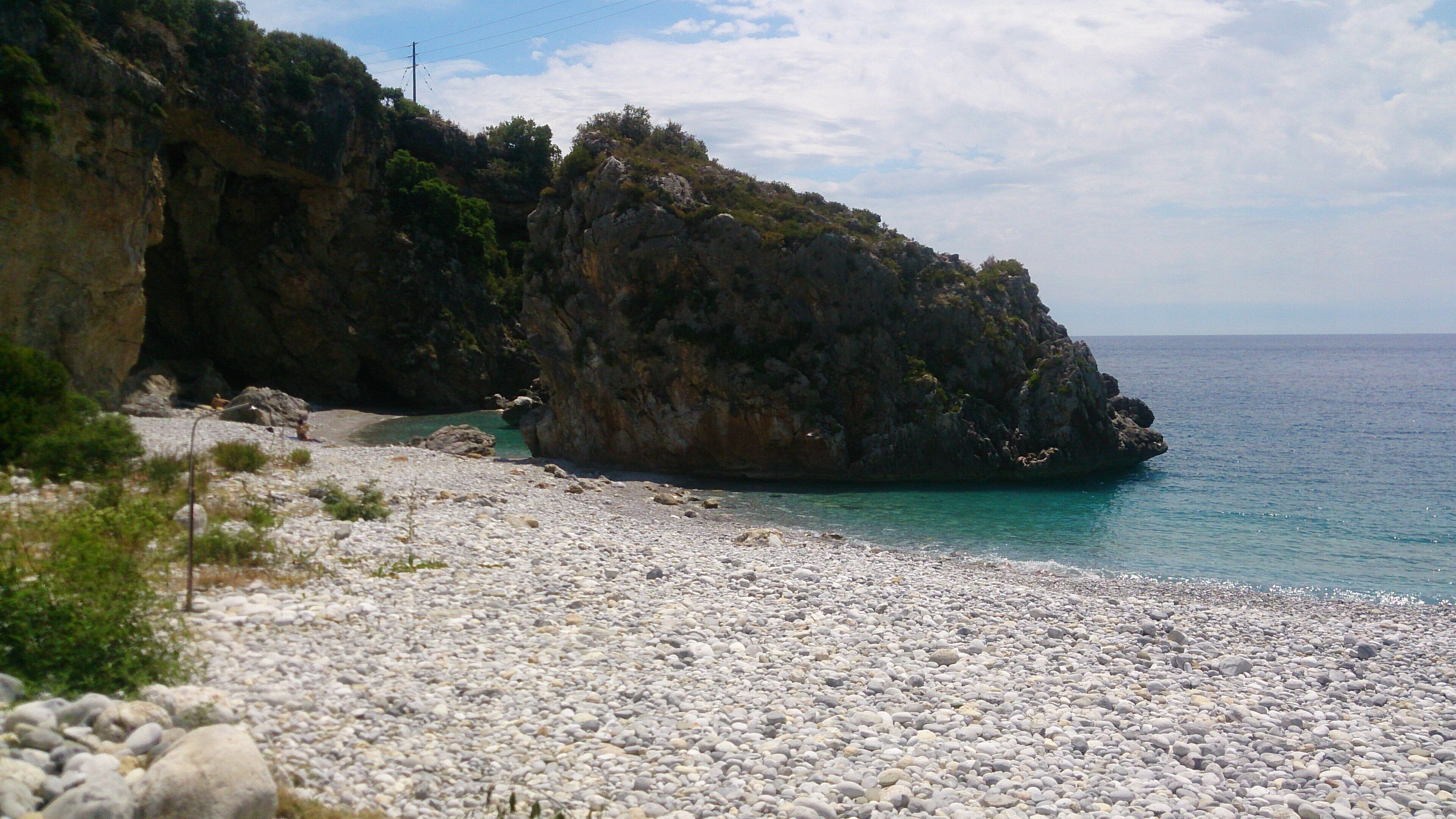 A rocky beach with a rugged cliff and calm sea.