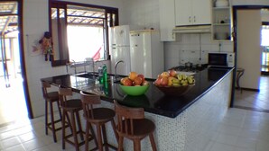 Una cocina con una isla central, taburetes de bar, un refrigerador, un microondas y un lavamanos.