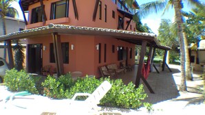 Un edificio de dos pisos con un patio techado, mesas al aire libre y un pequeño jardín.