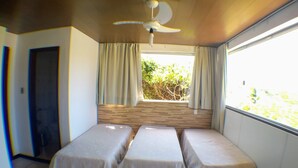Una habitación con dos camas individuales, ventilador de techo, ventana con cortinas y vistas al exterior.