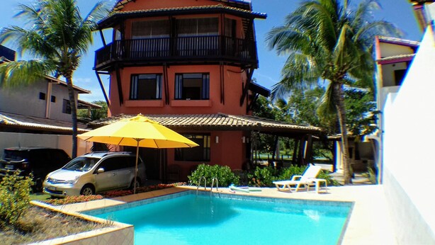 Un edificio de dos pisos con balcón, piscina y un automóvil estacionado.