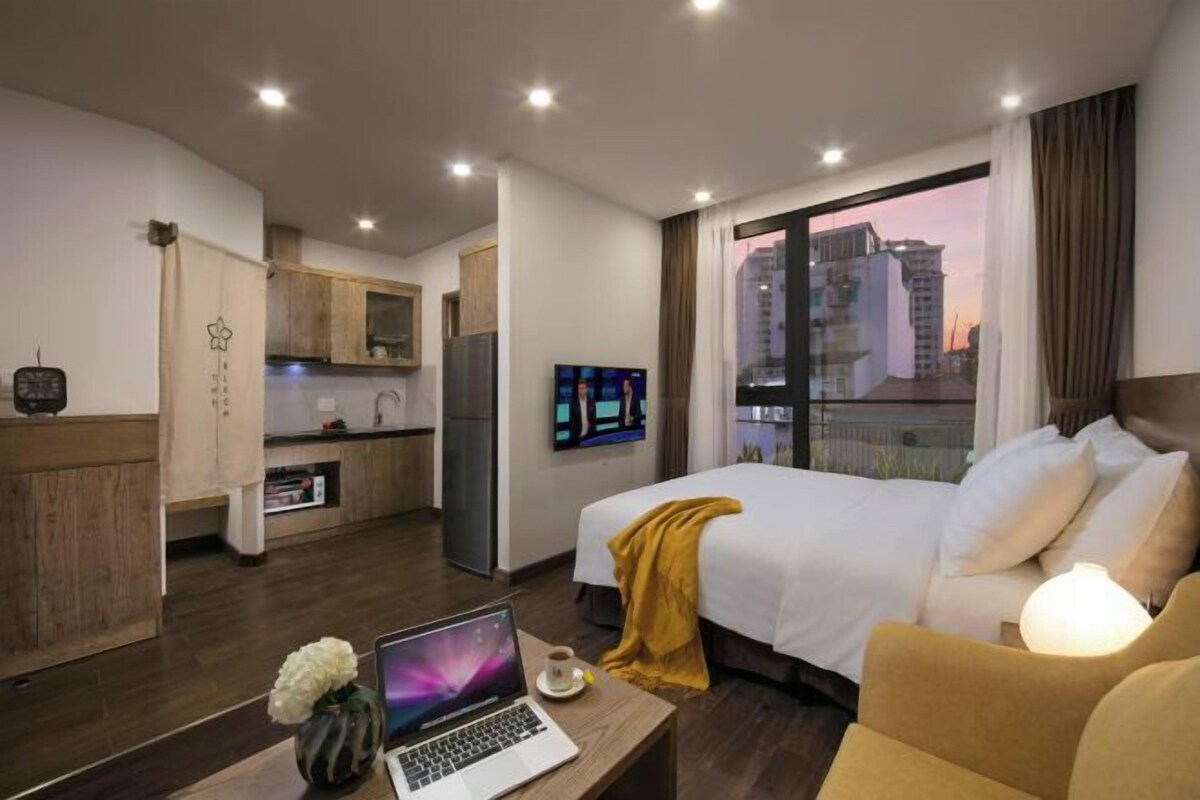 A hotel room with a bed, a sofa, a desk with a laptop, a TV, and a view of a cityscape.