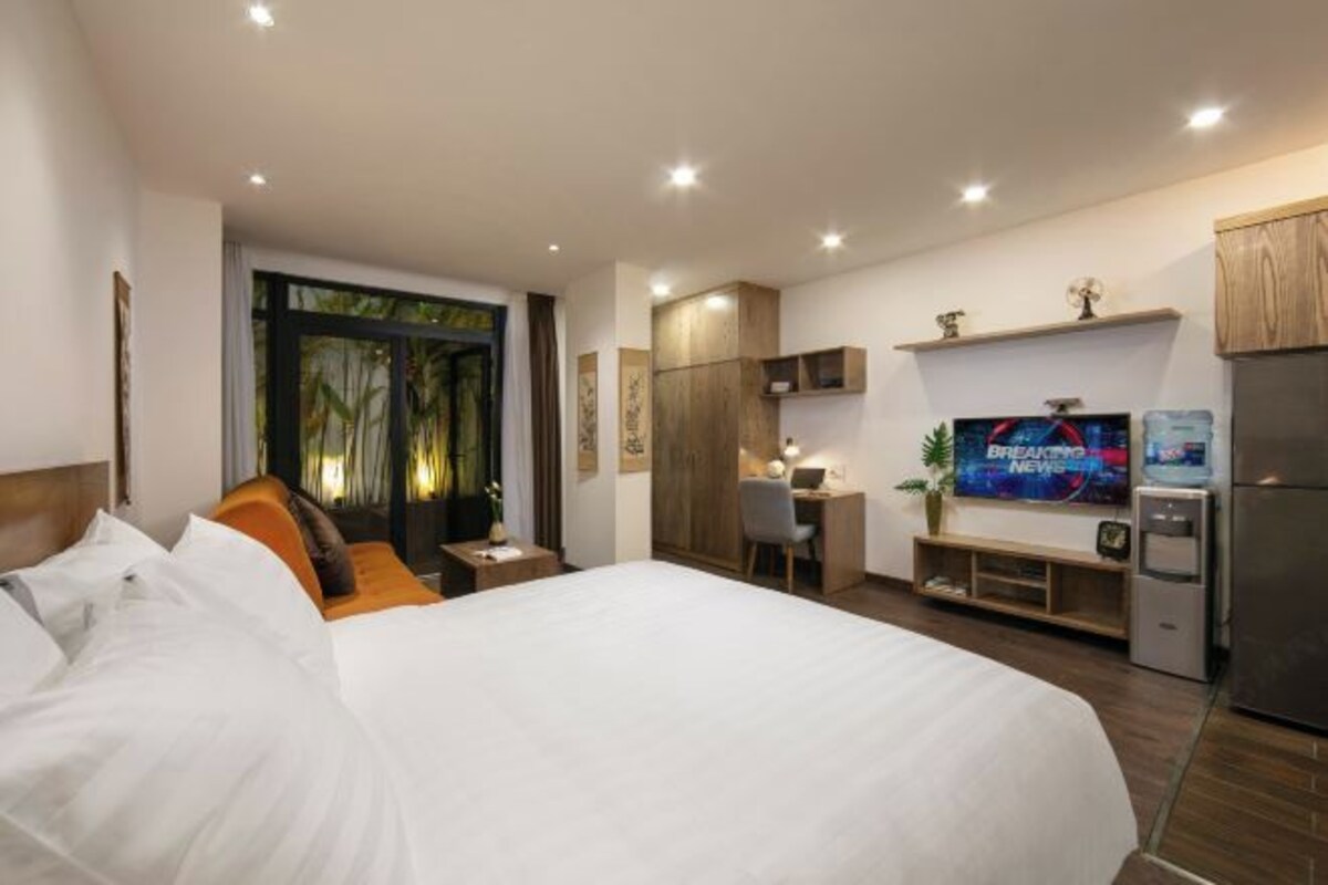 A hotel room with a large bed, a desk with a chair, a television, and a refrigerator.
