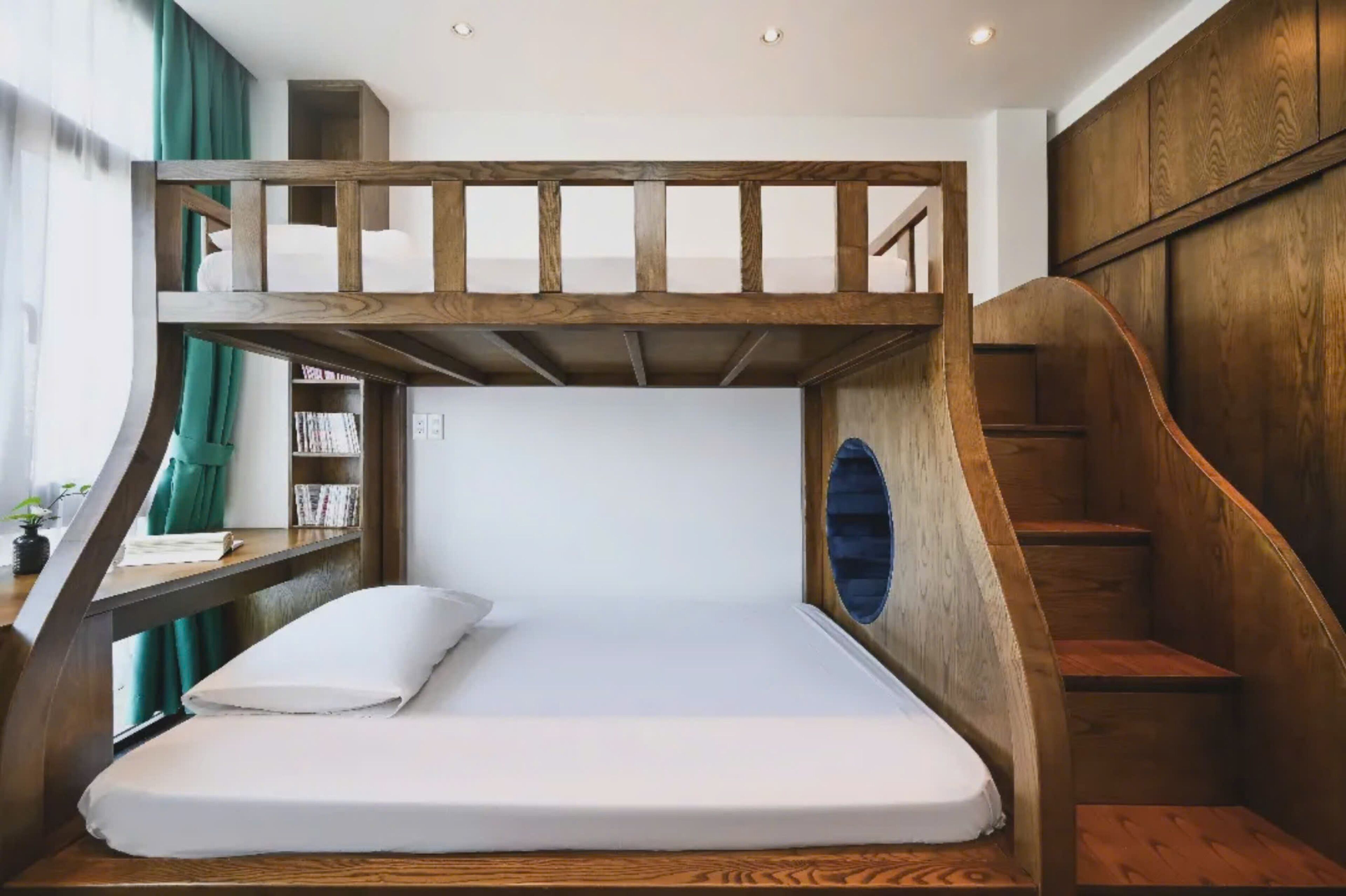 Una cama litera con estructura de madera, colchón blanco y una pequeña repisa con libros.