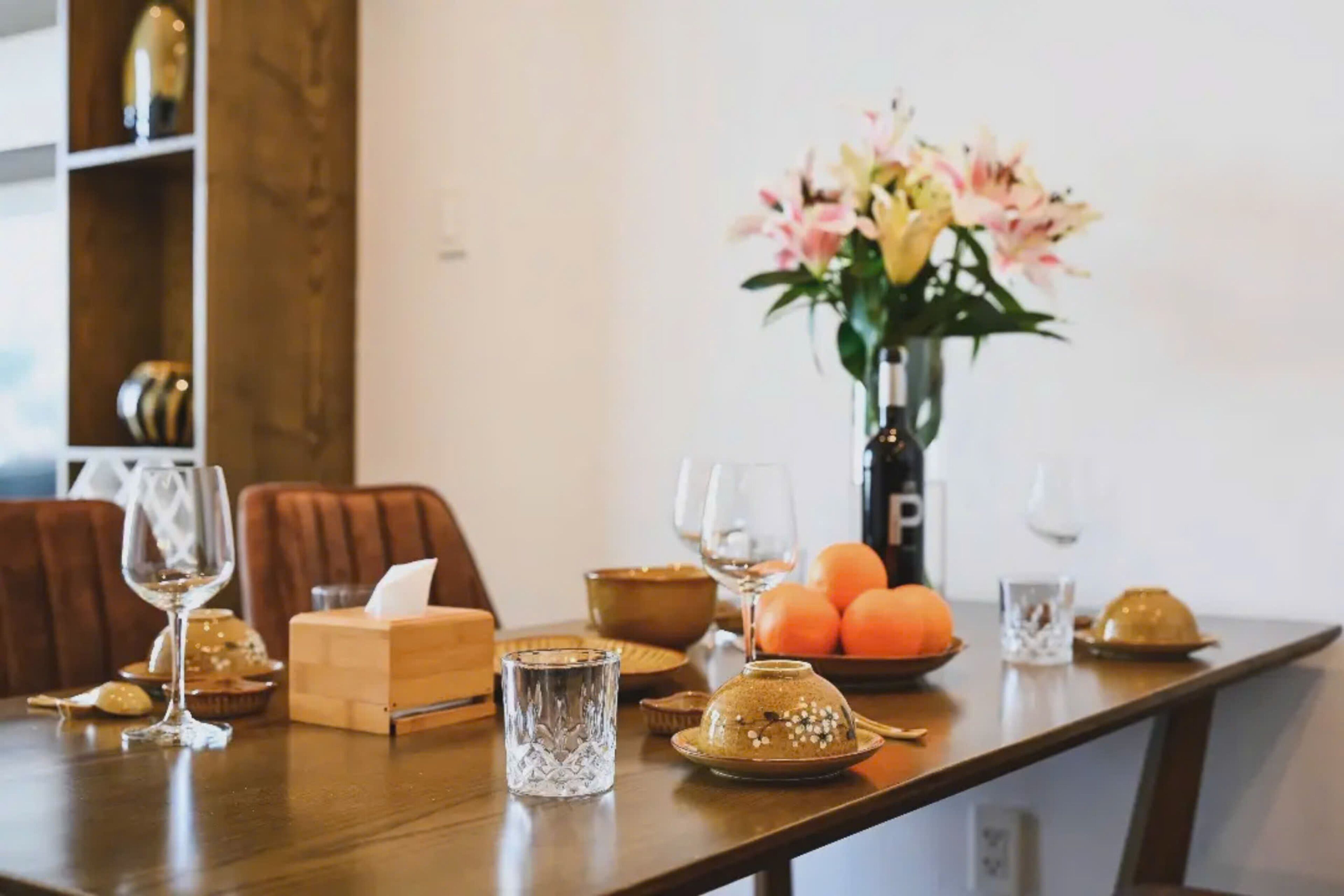 A dining table set with a vase of flowers, a bowl of oranges, and various glassware.