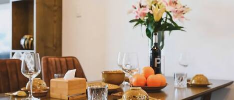 A dining table set with a vase of flowers, a bowl of oranges, and various glassware.