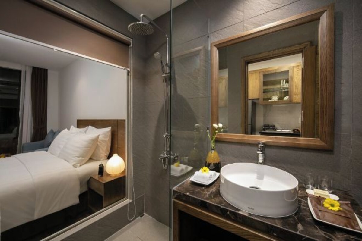 A modern hotel room with a bed, a bathroom with a large mirror, a sink, and a shower.
