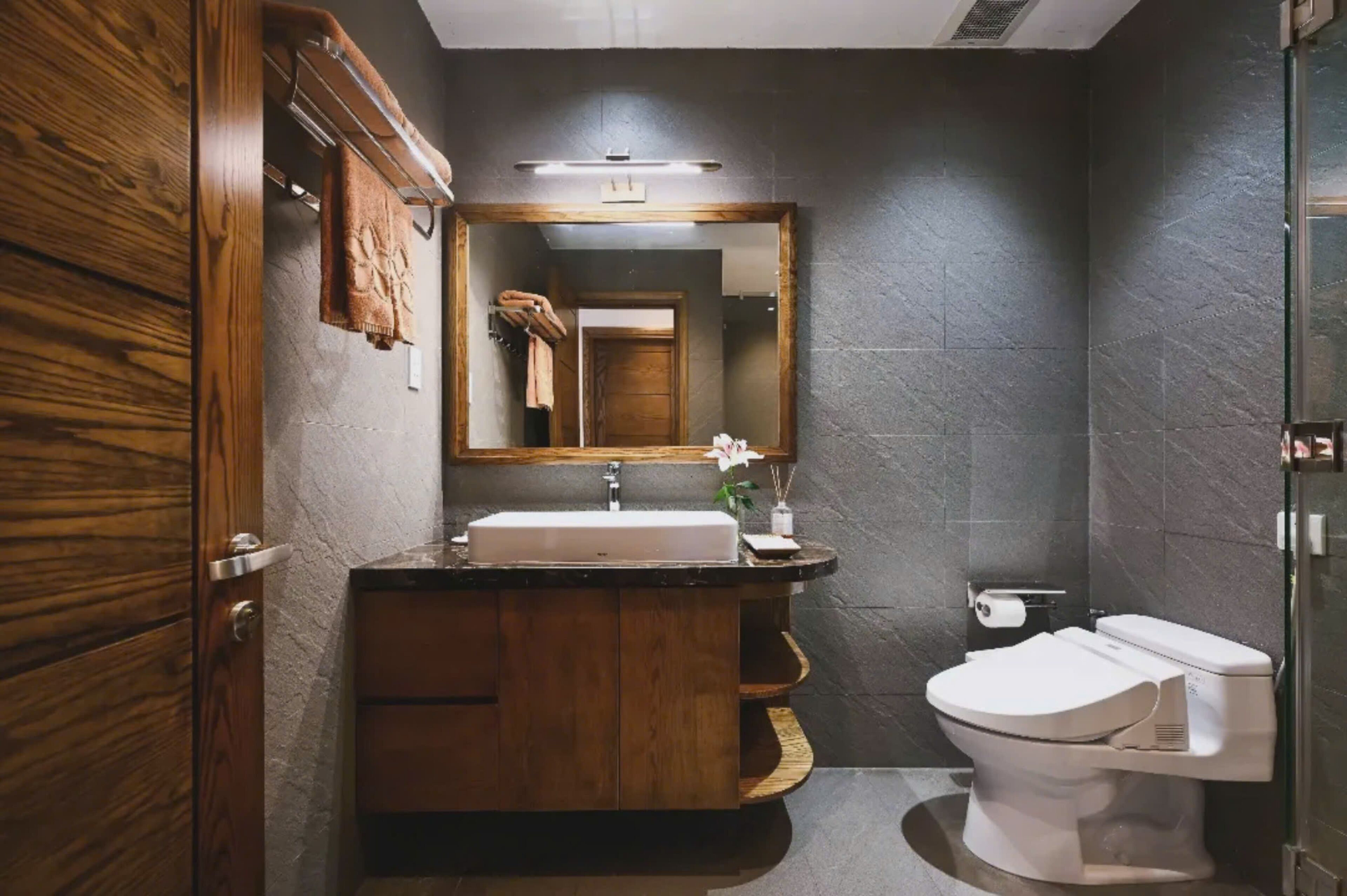 A modern bathroom with a wooden vanity, a large mirror, a white sink, and a toilet.