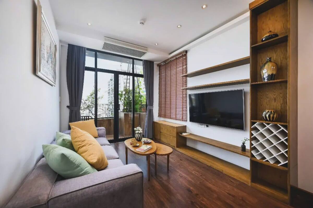 A modern living room with a sofa, coffee table, TV, and wooden shelving.