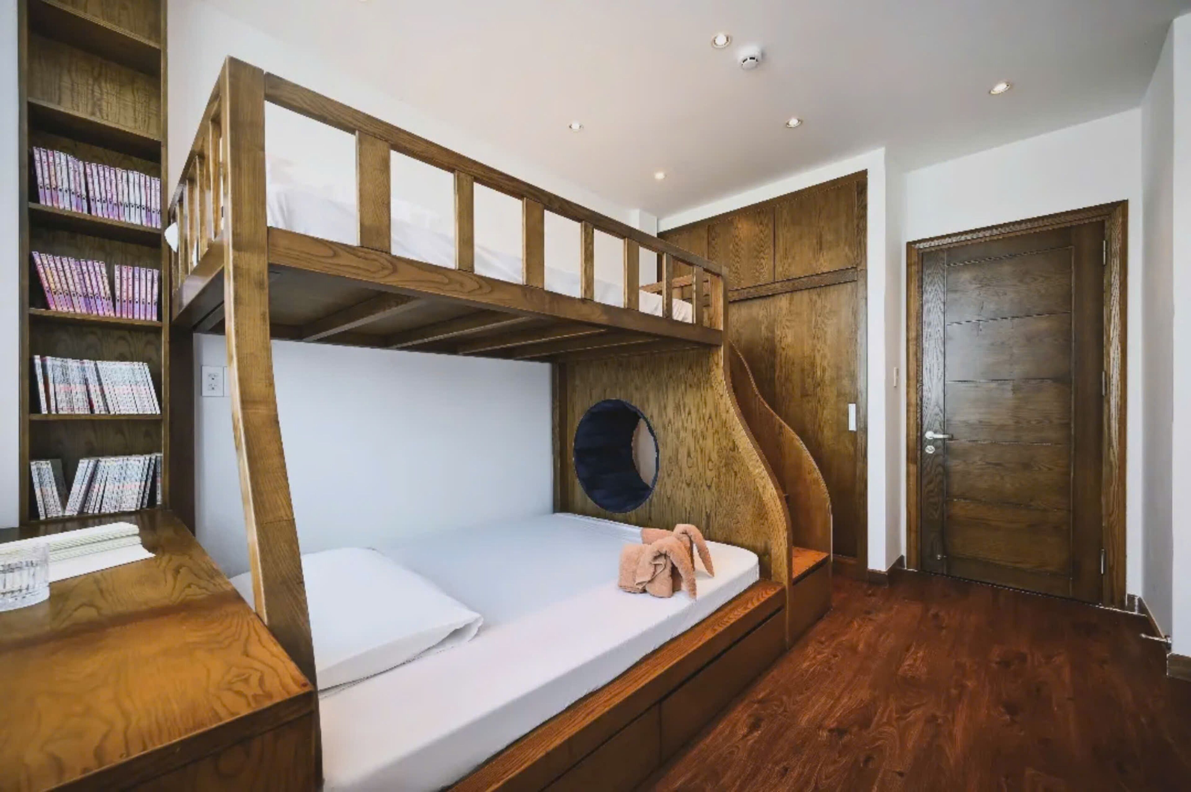 A bunk bed with a wooden frame, a bedside table with a glass, and a bookshelf with books.