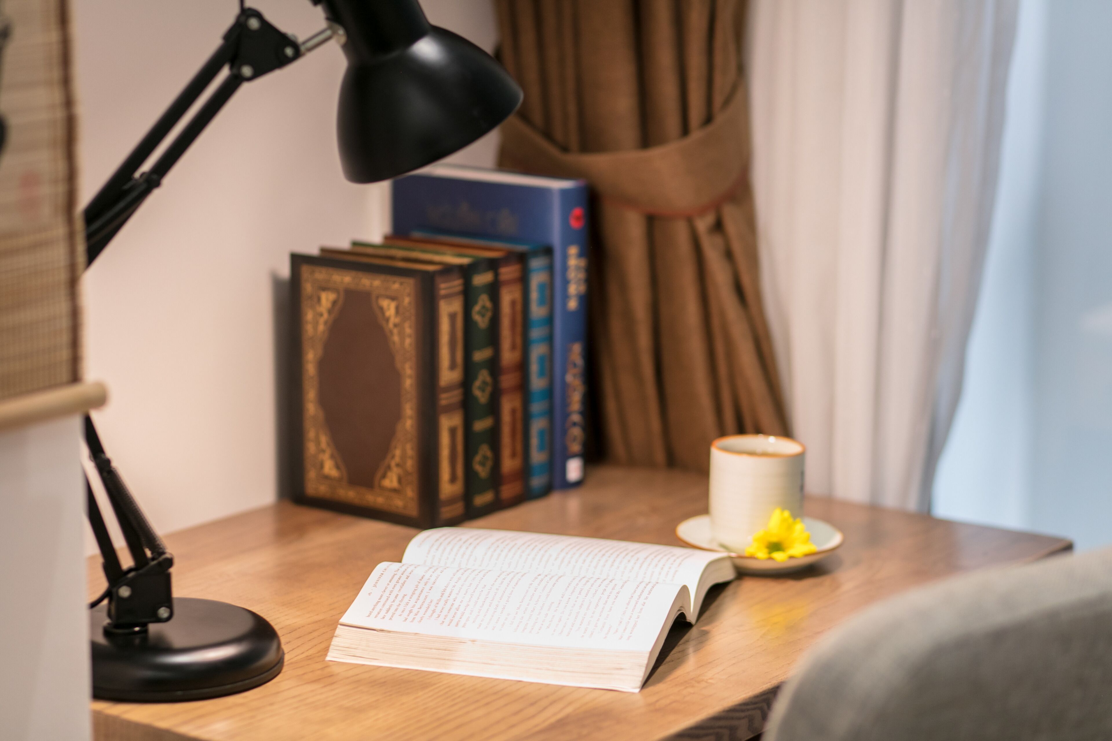 Une table de chevet en bois avec un livre, une lampe et une tasse de café.