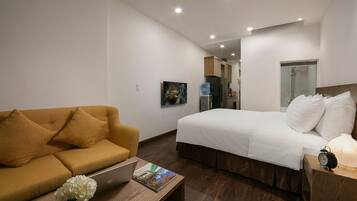 A hotel room with a bed, a sofa, a wooden coffee table, a laptop, and a water bottle.