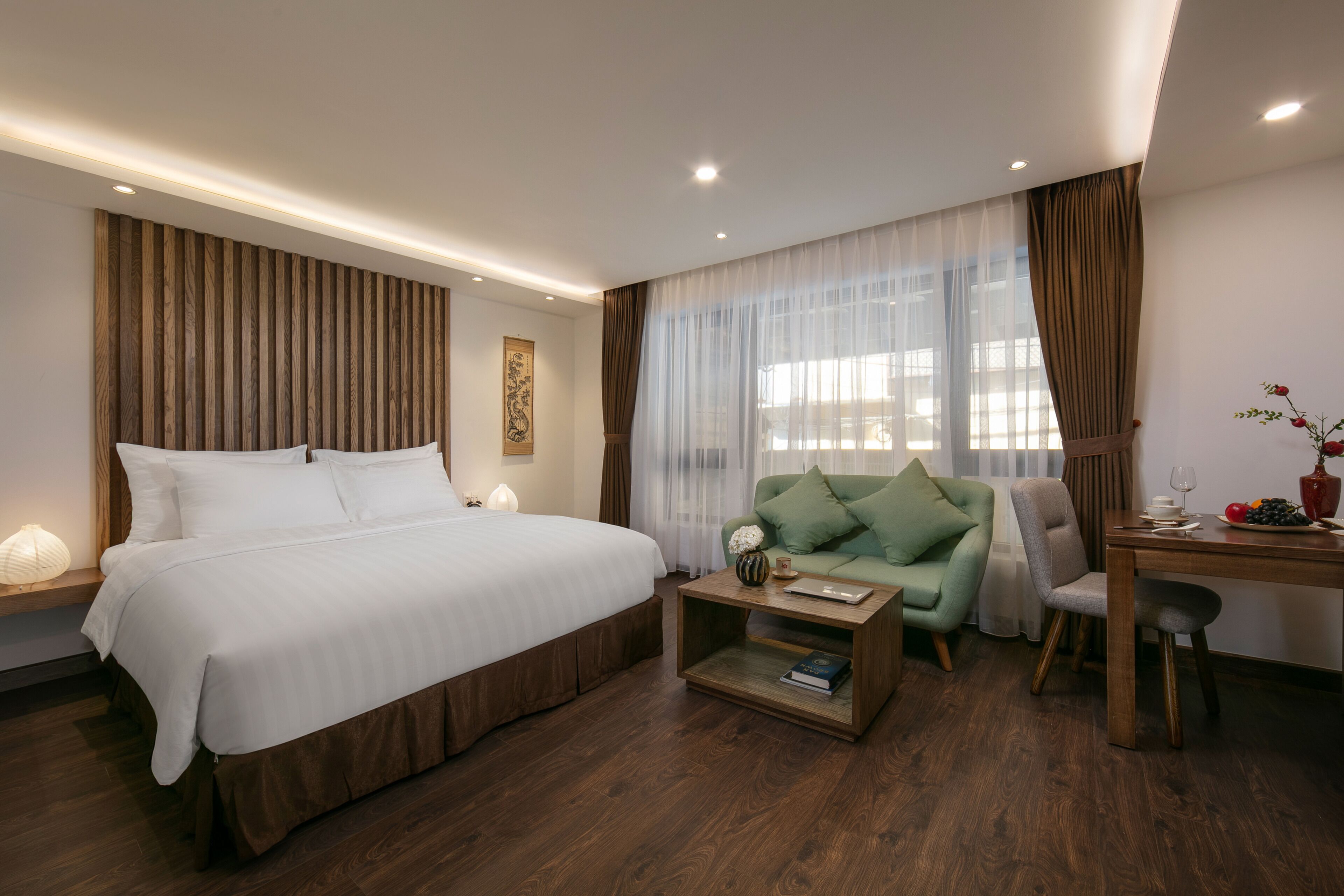 Ein modernes Hotelzimmer mit einem großen Bett, einem grünen Sofa, einem Holztisch und einem Schreibtisch mit Blumen.