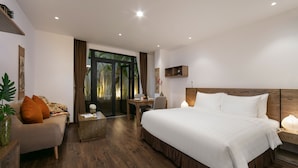 A modern hotel room with a large bed, a sofa, a small table, and a desk. There is a window with curtains and a view of greenery outside. - The Bloom Pham Viet Chanh - Modern Living Space in Saigon - A Top Choice for Western Travelers (Ho Chi Minh City)