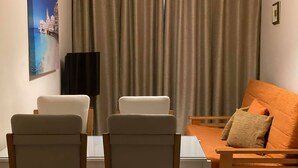 A living area with a sofa and two chairs, a flat-screen TV, and a painting on the wall.