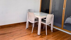 A small balcony with a glass table and wicker chairs, wooden flooring, and a sliding glass door.