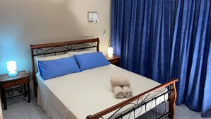 A neatly made bed with blue pillows, a wooden headboard, and a pair of rolled towels on the mattress.