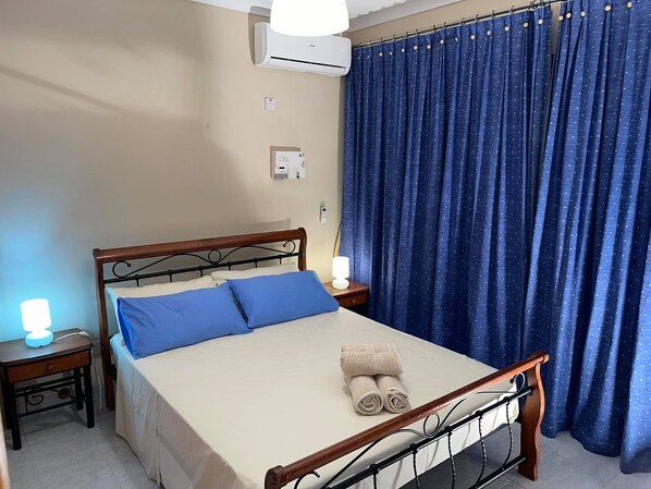 A neatly made bed with blue pillows, a wooden headboard, and a pair of rolled towels on the mattress.