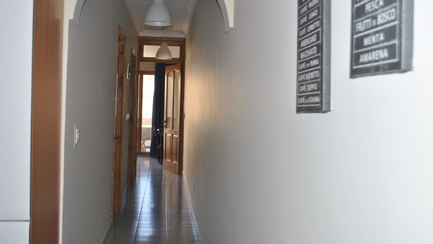 A hallway with a ceiling light, a door at the end, and a sign listing room amenities.