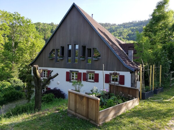 Une maison à deux étages, avec un toit en pente, un revêtement en bois et des volets rouges.