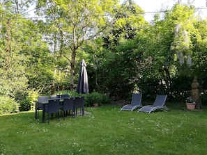 Un espace extérieur verdoyant, avec une table et des chaises, entouré d’arbres et agrémenté d’un parasol suspendu.