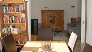 Een eetgedeelte met een houten tafel, stoelen, een kroonluchter, een boekenkast en een televisie op de achtergrond.