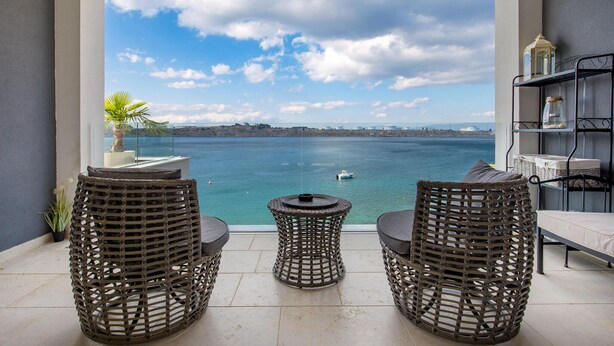 A balcony with wicker chairs and a small table, overlooking a body of water with a boat and distant shoreline. - Cozy apartment in Omisalj with house sea view (Omisalj)